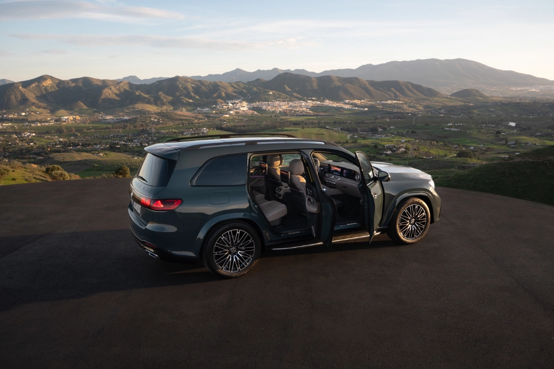 Mercedes GLS 2026 verde con portiere aperte vista di tre quarti posteriore, panorama collinare al tramonto