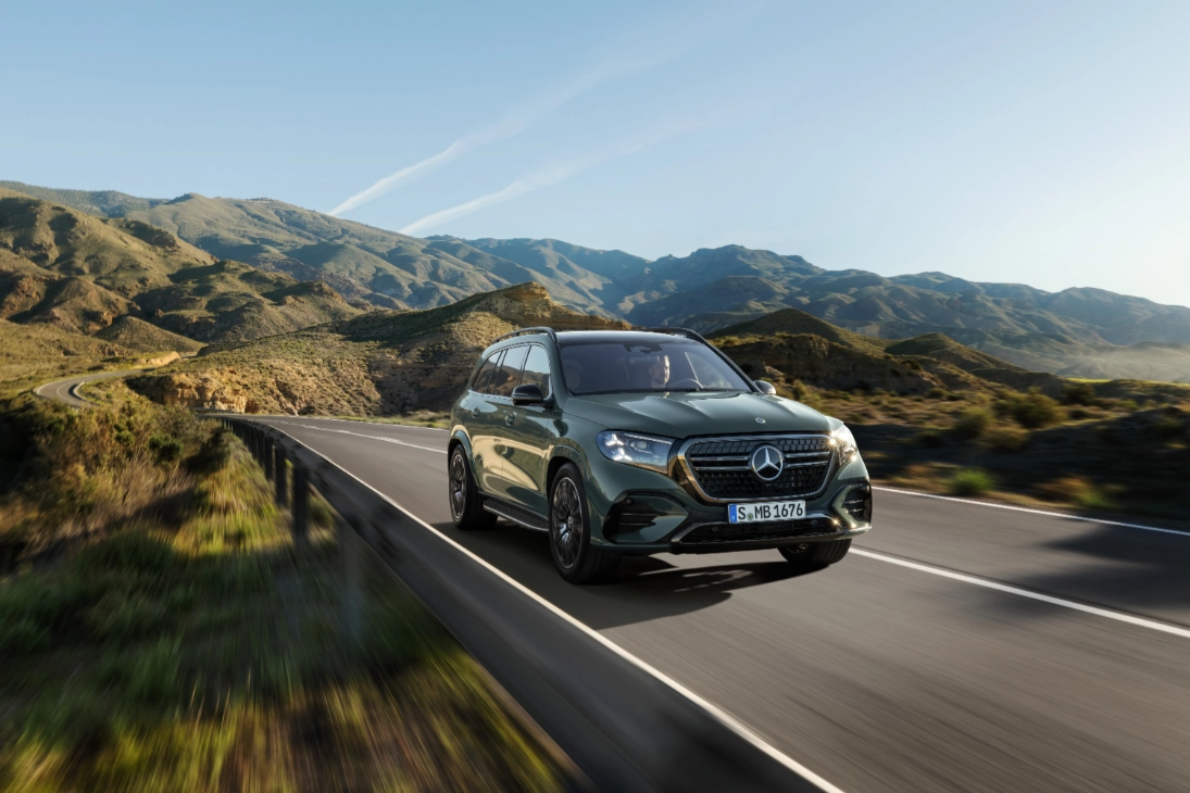 Mercedes GLS 2026 verde in movimento su strada di montagna, vista di tre quarti anteriore con calandra a stelle e fari DIGITAL LIGHT accesi
